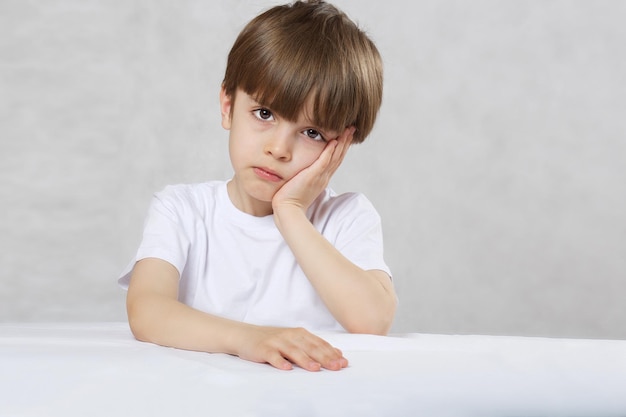 Niño de seis años en camiseta blanca en la mesa. De cerca