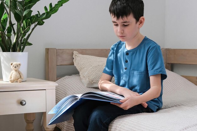 Un niño de seis años está leyendo un libro mientras está sentado en la cama Educación en el hogar Preparación para la escuela