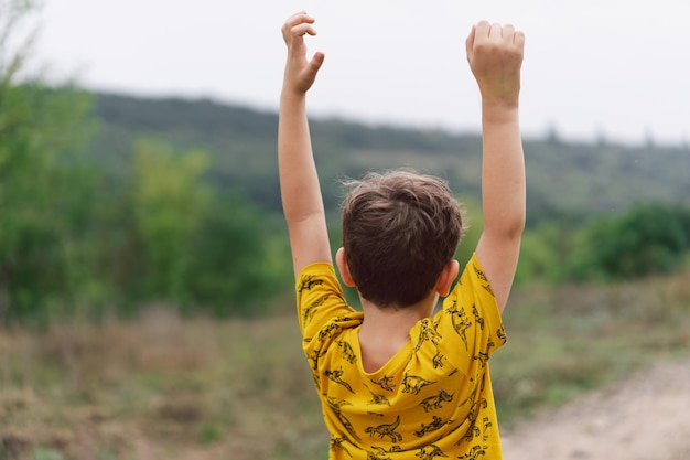 Un niño de seis años está de pie con la espalda en el campo Vista posterior Niño feliz riendo y jugando en el día de verano