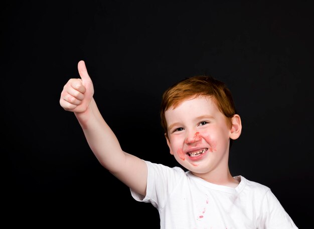 un niño de seis años con fresas rojas maduras, un niño pequeño que se untó la cara y la ropa con fresas mientras comía