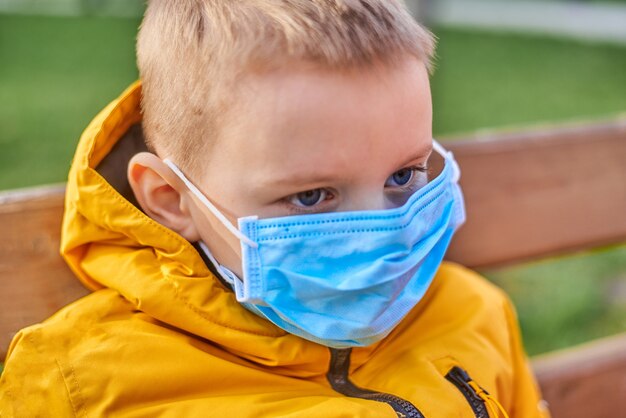 Niño de seis años con una máscara médica en una calle en primavera