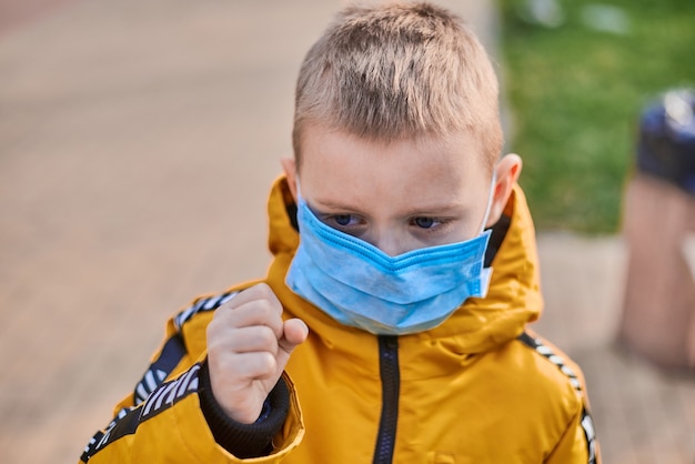 Niño de seis años con una máscara médica en una calle en primavera