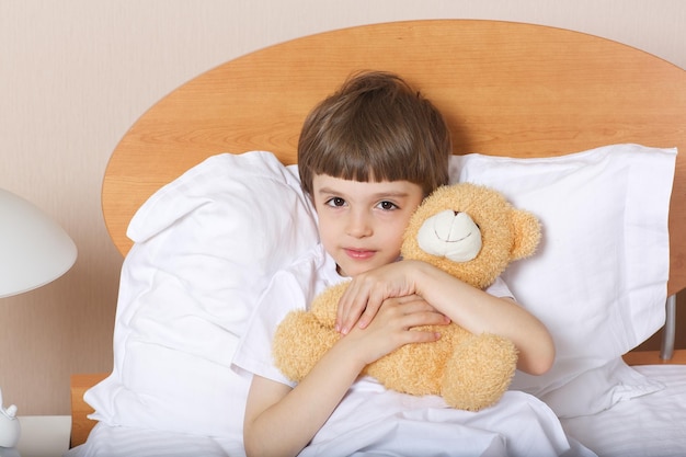Niño de seis años con osito de peluche en su cama. De cerca