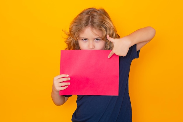 Niño señalando en una hoja de papel vacía aislada sobre fondo amarillo retrato de un niño sosteniendo un espacio en blanco