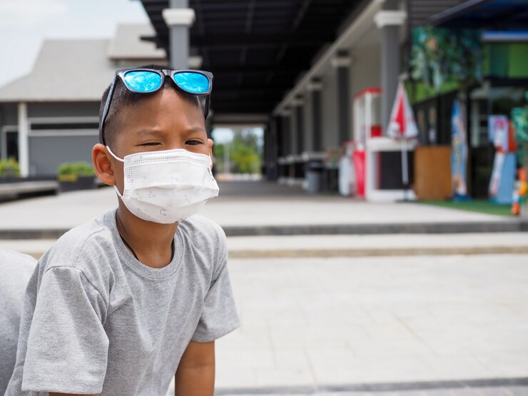 Foto niño sentado afuera con una máscara protectora