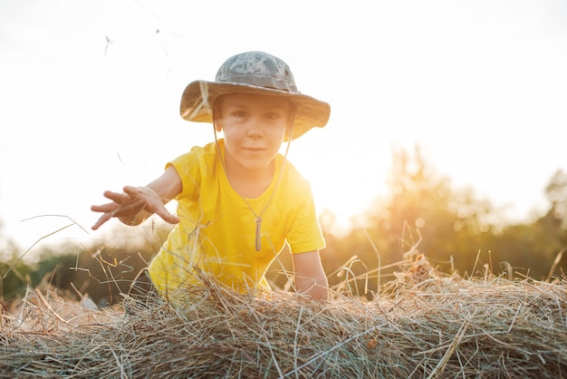 Foto niño sentado a la altura de un gran pajar en el pueblo. el niño el granjero.