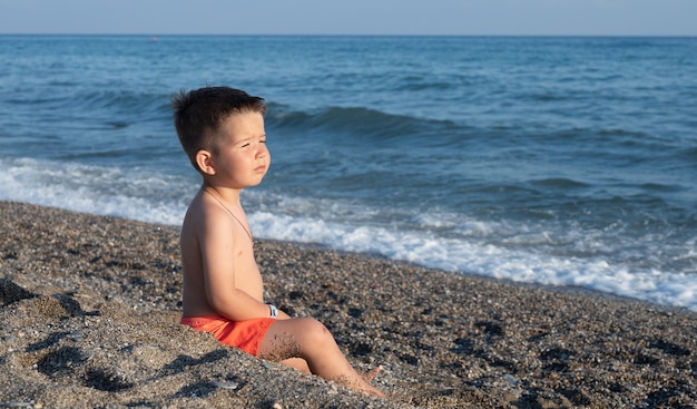 Niño sentado en la arena y mirando al mar.