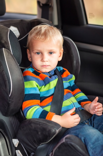 Niño sentado en un asiento de seguridad abrochado en el coche.