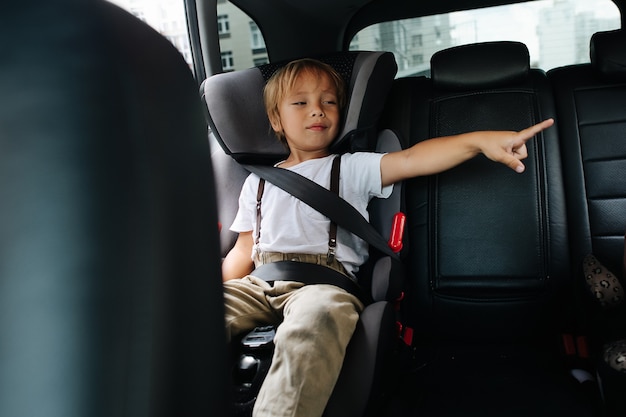 Niño sentado en un asiento de seguridad para niños en un automóvil, apuntando hacia un lado. Desde el interior de un salón.