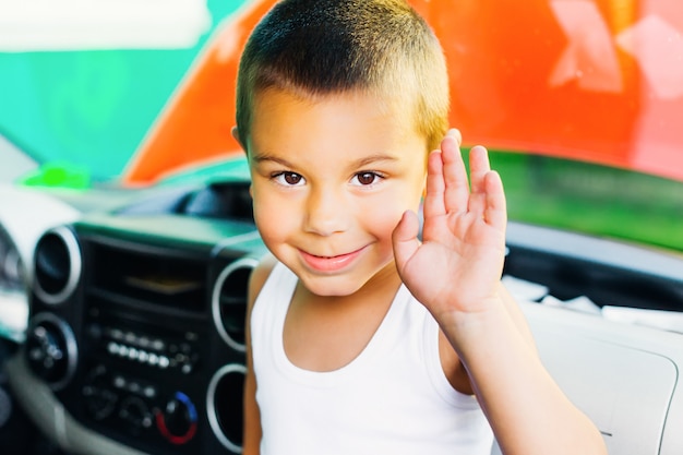 Niño sentado en el auto y sonriendo y agitando su mano