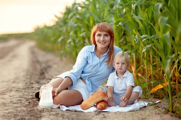 Niño sentado en un campo de maíz con mamá en un picnic