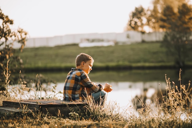 Niño sentado cerca de un estanque de río o lago y sonriendo Temporada de otoño Infancia feliz