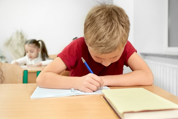 Niño sentado en el escritorio, escribiendo con lápiz en cuaderno.
