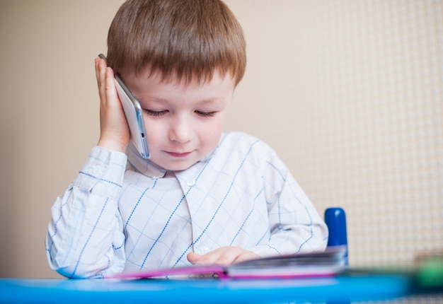 Niño sentado en el escritorio y hablando por teléfono