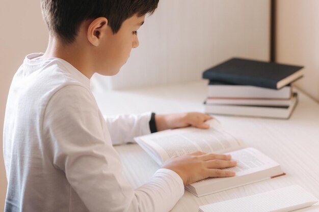 Niño sentado en el escritorio y leyendo el libro Estudiar en casa durante la cuarentena