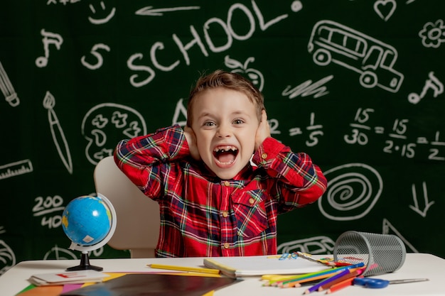 niño sentado en el escritorio con muchos útiles escolares