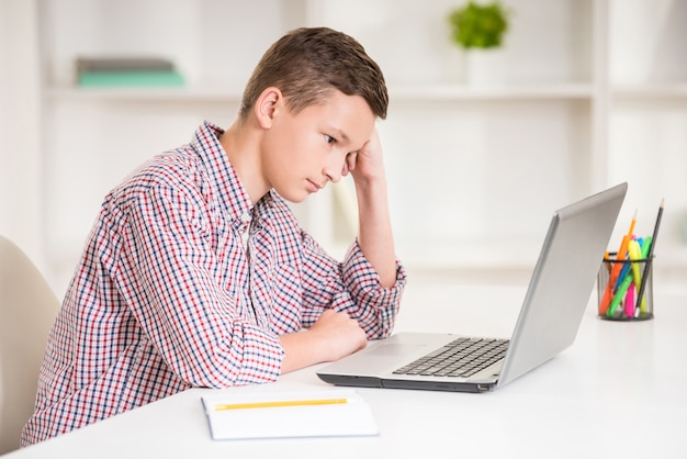 Niño sentado en el escritorio con ordenador portátil y hacer la tarea.