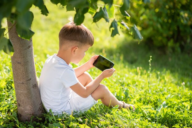 niño sentado en la hierba mirando por teléfono