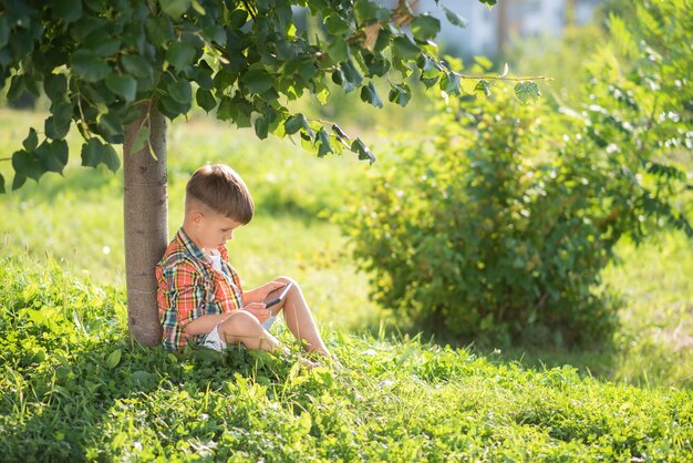 niño sentado en la hierba mirando por teléfono