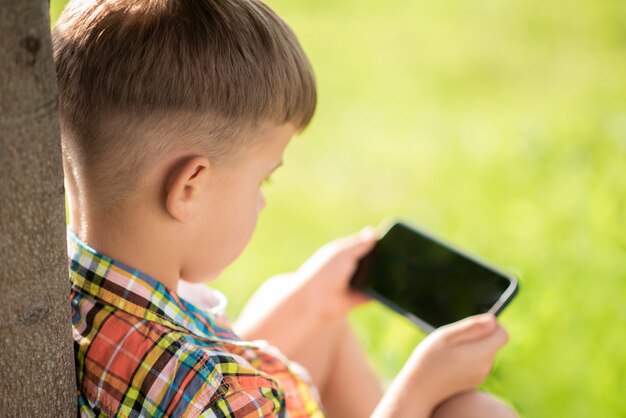 niño sentado en la hierba mirando por teléfono