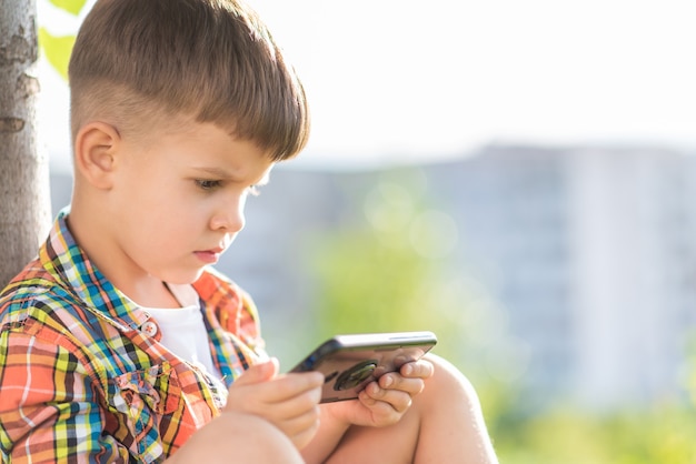 Foto niño sentado en la hierba mirando por teléfono