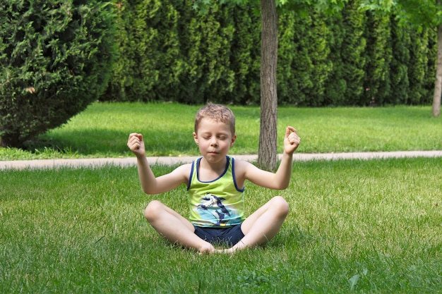 Foto el niño está sentado en la hierba en posición de loto.