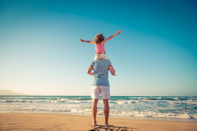 Niño sentado en el hombro del padre en la playa con fondo de cielo y mar