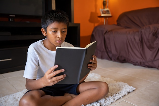 Niño sentado leyendo en la sala de estar en casa