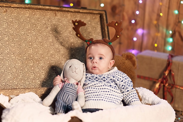 Niño sentado en una maleta con un juguete en la habitación con adornos navideños