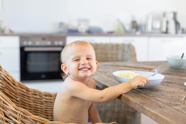 Niño sentado a la mesa en una cocina y comiendo espaguetis con queso. Niño tomando el almuerzo. Concepto de comida sana para niños.