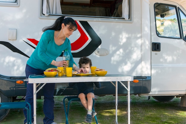 niño sentado en la mesa junto a la caravana mientras su madre sirve sándwiches y bebidas