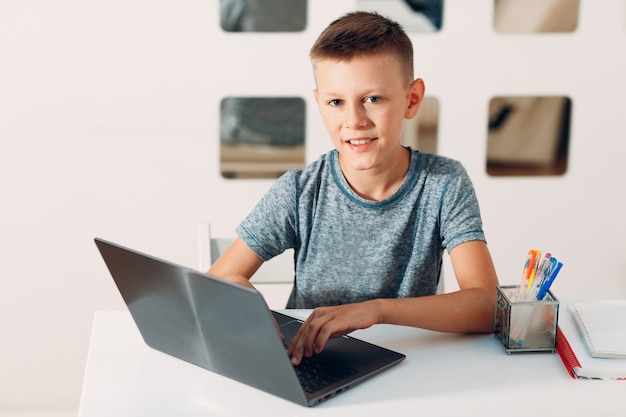 Niño sentado a la mesa con el portátil y preparándose para la escuela en casa