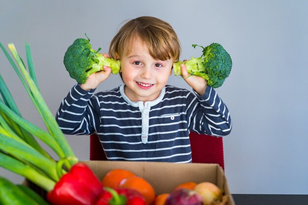 Foto niño sentado a la mesa y tomando brócoli