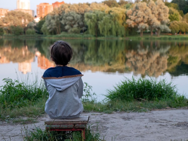 Foto niño sentado a la orilla de un lago persona sentada en un banco sola y viendo la puesta de sol