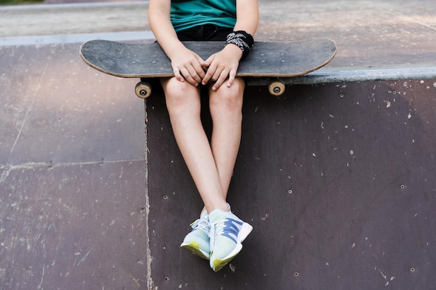 Niño sentado con patineta en primer plano Equipo deportivo para niños Adolescente activo con parque infantil en el parque de patinaje