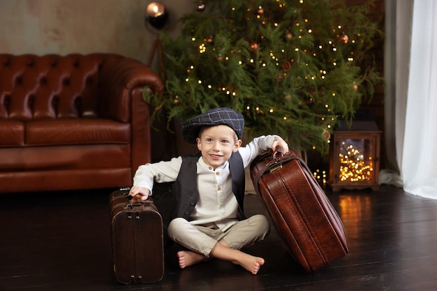 Niño sentado en el piso con maleta de navidad en el salón