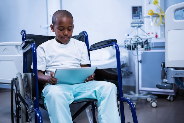 Niño sentado en silla de ruedas y usando tableta digital en sala
