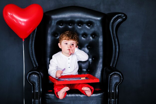 Niño sentado en el sillón con cuadro rojo enmarcado en el día de San Valentín.