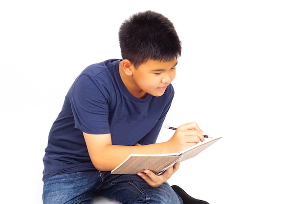 Niño sentado sobre fondo blanco y escribiendo un libro Concepto de educación y aprendizaje