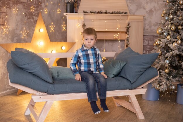 Niño sentado en el sofá junto a la chimenea. Concepto de temporadas de Navidad, año nuevo, invierno y vacaciones.