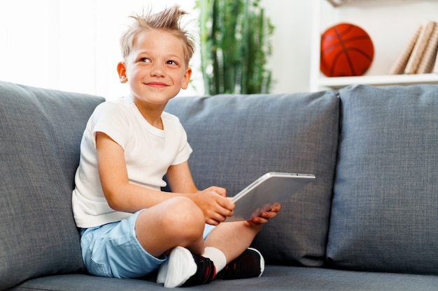 Niño sentado en el sofá y usando tableta digital en casa