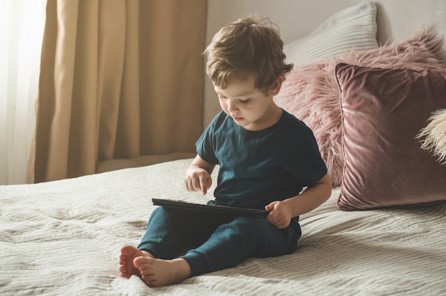 Niño sentado con una tableta en la cama