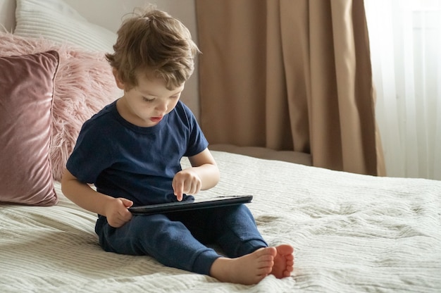 Niño sentado con una tableta en la cama