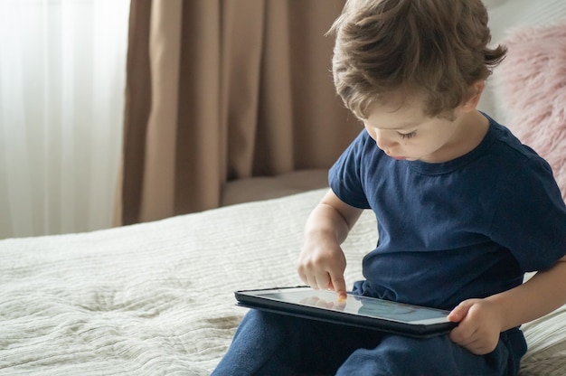 Niño sentado con una tableta en la cama