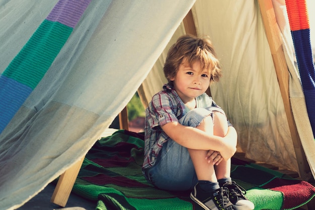 Niño sentado en una tienda de campaña en un campamento de verano campamento sueño niño sueños en una tienda al aire libre infancia sueño soñar despierto