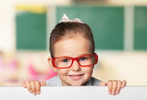 Niño serio con gafas de marco rojo mirando hacia arriba desde detrás de la mesa en primer plano