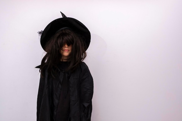 Foto niño serio de halloween sobre fondo blanco que cubre su rostro con su cabello niño en traje de hechicero negro con cabello largo truco de bruja misterioso o trato alegre niño en traje mago espacio de copia