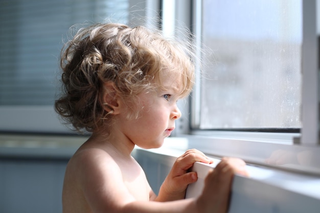 Niño serio mira atentamente por la ventana profundidad de campo