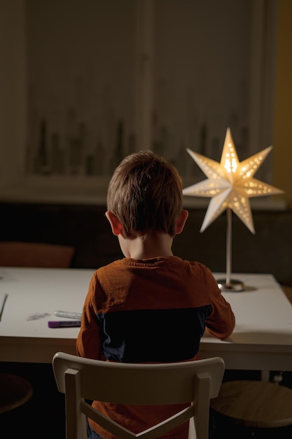 un niño se sienta al lado de una lámpara en forma de estrella con patrones en la noche