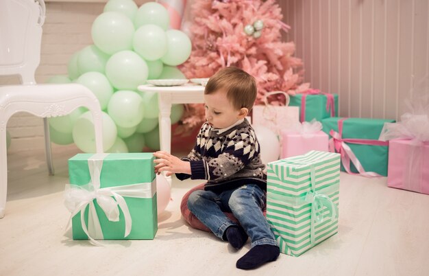 Un niño se sienta en una almohada y desempaqueta los regalos con el telón de fondo de un árbol de Navidad